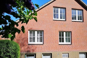 Ein rotbacksteins Gebäude mit vielen Fenstern, einem grünen Heckenstreifen und einem strahlend blauen Himmel.