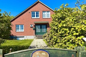 Ein zweistöckiges Ziegelhaus mit grüner Tür und Fenstern, einer sichtbaren Garage und einem gepflegten Rasen.