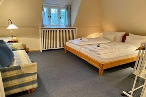 Et soveværelse med en enkelt seng, en lille sofa, en radiator og et vindue med gardiner.