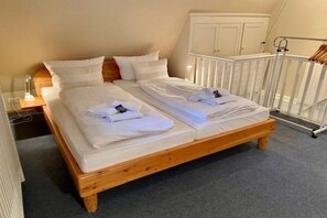 A double bed with white linens and towels, a wooden headboard, a white crib, and a white wardrobe in a bedroom. - Dream Street Bollis Huis 2 (Nieblum)