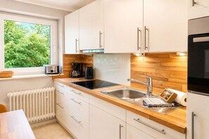 Eine moderne Küche mit weißen Schränken, einer Holz Arbeitsplatte, einer schwarzen Induktionskochplatte, einer Edelstahl-Spüle und einem Fenster mit Blick auf Grünflächen.