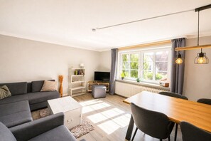 A modern living room with a sofa, a dining table, and a TV. - Holiday apartment with 1 bedroom (Wyk auf Föhr)
