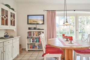 A dining area with a round table, chairs, a bookshelf, and a television. - Holiday home with 1 bedroom (Wrixum auf Föhr)