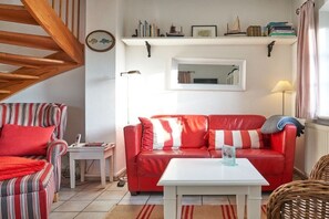 Un salón con sofá rojo, sillón a rayas, una mesa de centro blanca y una mesita auxiliar.