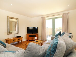 A living room with a television, wooden furniture, and a view of the outdoors. - Elm Cottage (Truro)
