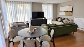 A modern living room with a sofa set, a dining table with chairs, a flat-screen TV, and a painting on the wall. - Southeast London 3-bed Apt, Sleeps 6 w Lake Access (London)