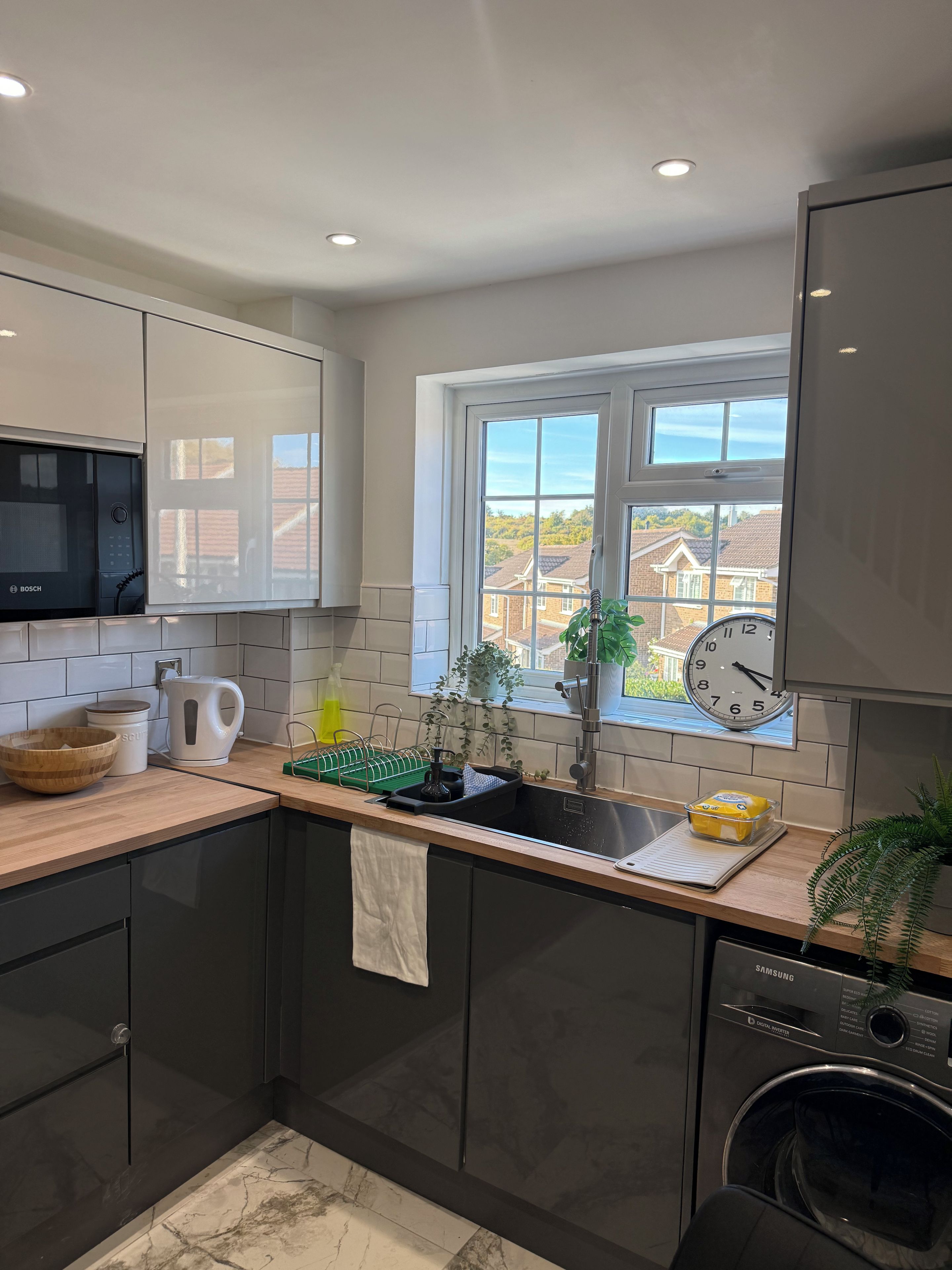 A modern kitchen with a Bosch microwave, a Samsung dishwasher, and a window with a view of houses.