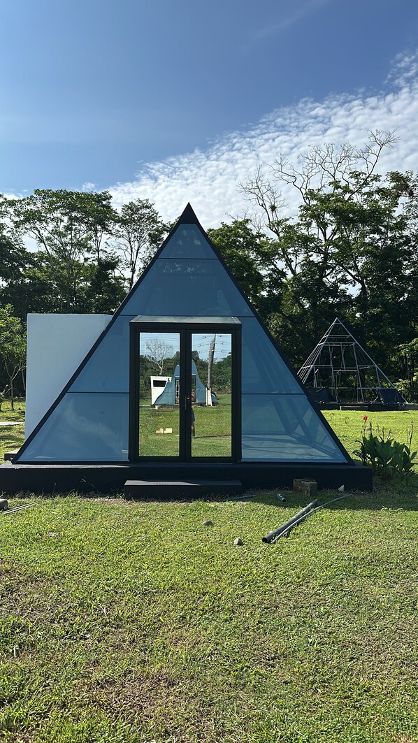 A modern glass pyramid structure with a reflective surface, surrounded by a grassy area and trees.