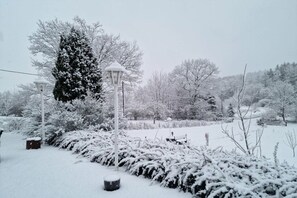 Jardim coberto de neve com um banco, um lampião e uma árvore coberta de neve.