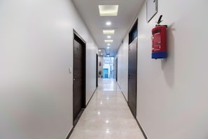 A corridor with doors on both sides, a fire extinguisher mounted on the wall, and a ceiling with recessed lighting.