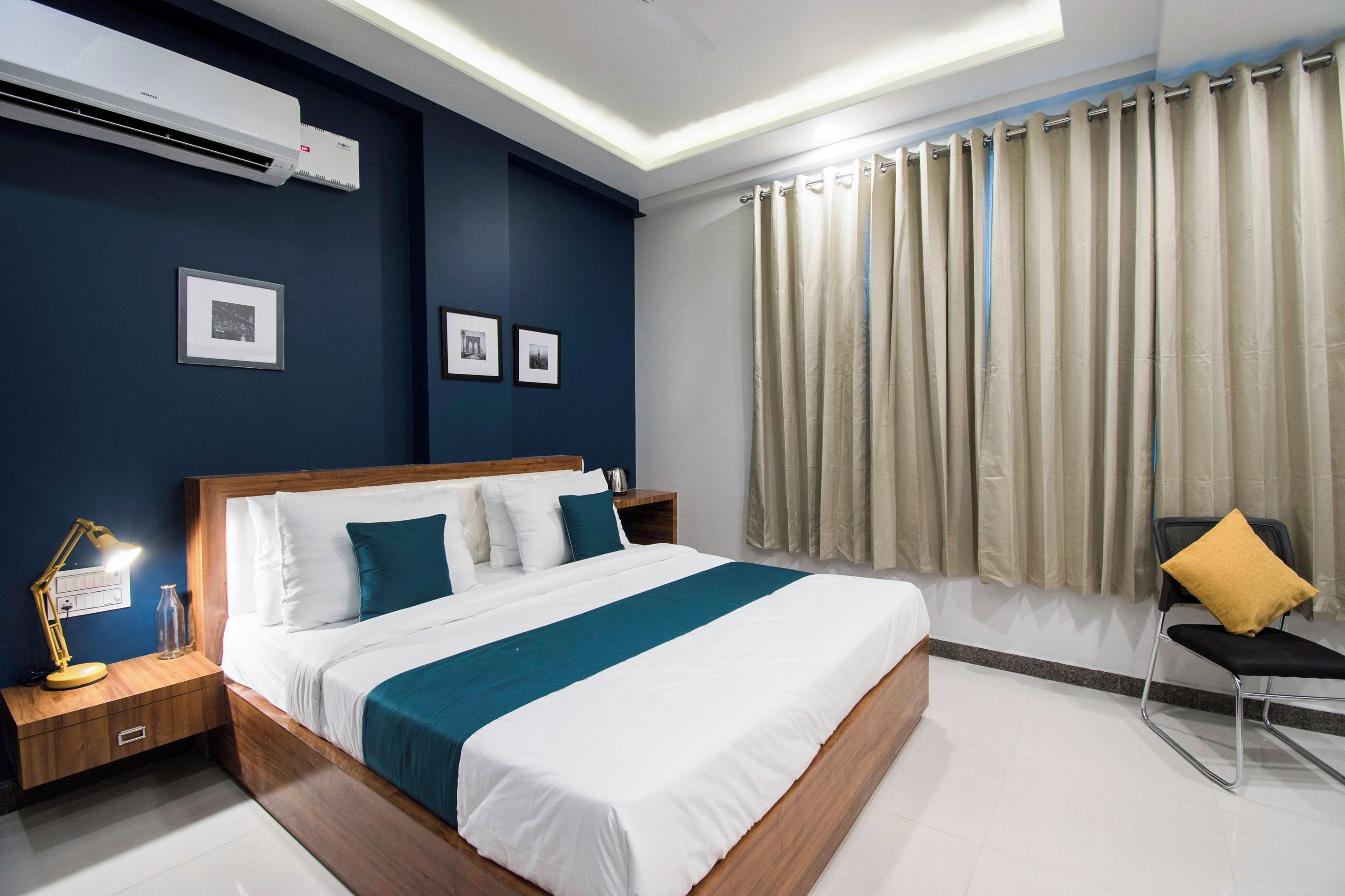 A modern hotel room with a large bed, bedside tables, a desk with a lamp, a chair, and a window with curtains.