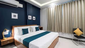 A modern hotel room with a large bed, bedside tables, a desk with a lamp, a chair, and a window with curtains.