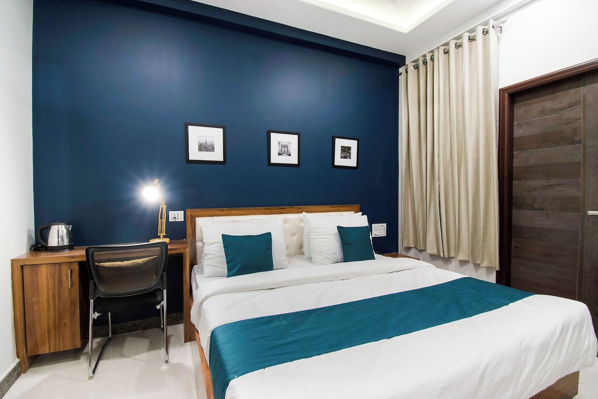 A hotel room with a bed, a desk, a chair, and three framed pictures on the wall.