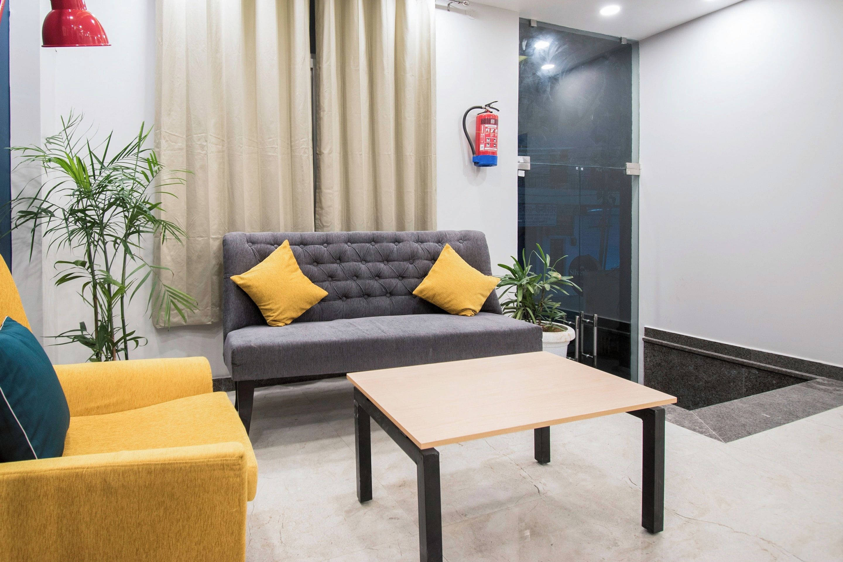 Un vestíbulo moderno con un sofá gris, cojines amarillos, una mesa de centro de madera y plantas en macetas.
