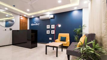 A reception area with a reception desk, a seating area with a sofa and armchair, a coffee table, and a wall-mounted air conditioning unit.