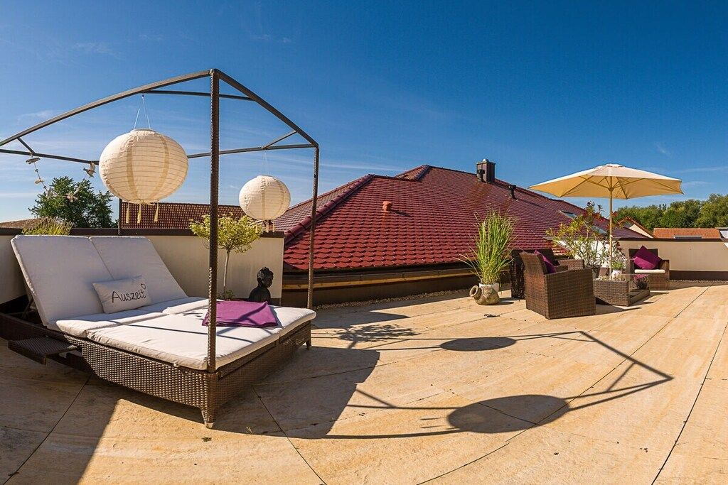 A rooftop terrace with a wicker sofa, a hanging lantern, and a yellow umbrella.