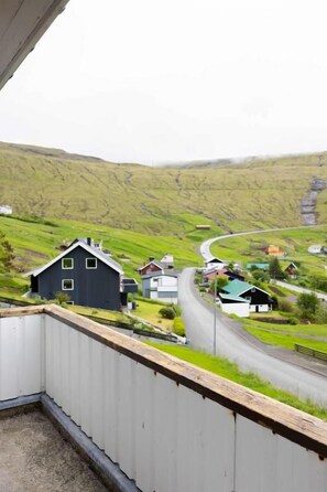A rural landscape with a road curving through green fields, houses, and a prominent rock formation in the distance.