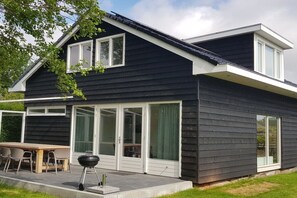 A modern two-story house with a dark exterior, large sliding glass doors, and a patio with outdoor furniture. - Holiday apartment with 1 bedroom (Julianadorp aan Zee)