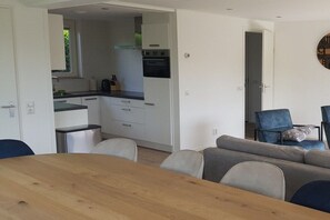 A compact living space with a kitchenette, a dining area with a wooden table, and a seating area with a sofa and chairs. - Holiday apartment with 1 bedroom (Julianadorp aan Zee)