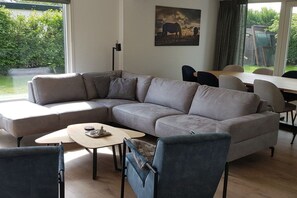 A modern living room with a sectional sofa, a small coffee table, and a dining area with chairs. - Holiday apartment with 1 bedroom (Julianadorp aan Zee)