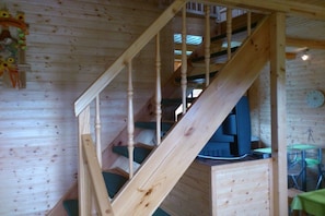 Una escalera de madera lleva a una zona superior con televisión y una mesa de comedor.