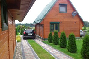 Ein Holzhaus mit geneigtem Dach, einer Satellitenschüssel und einer gepflasterten Auffahrt zu einem parkenden Auto.