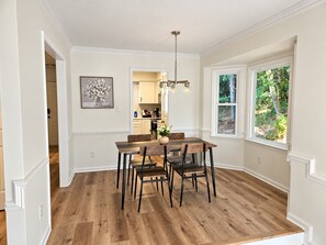 Een eetruimte met een houten tafel en stoelen, een hanglamp en uitzicht op het landschap door een raam.