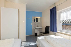 A hotel room with two beds, a bathroom with a sink, and a window with curtains. - Groepshuis Oase (12 people) (Zoutelande)