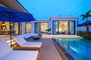 A modern outdoor pool area with lounge chairs, a dining setup, and a large umbrella. - Kata  Luxury 4-Bedroom Villa (Karon)