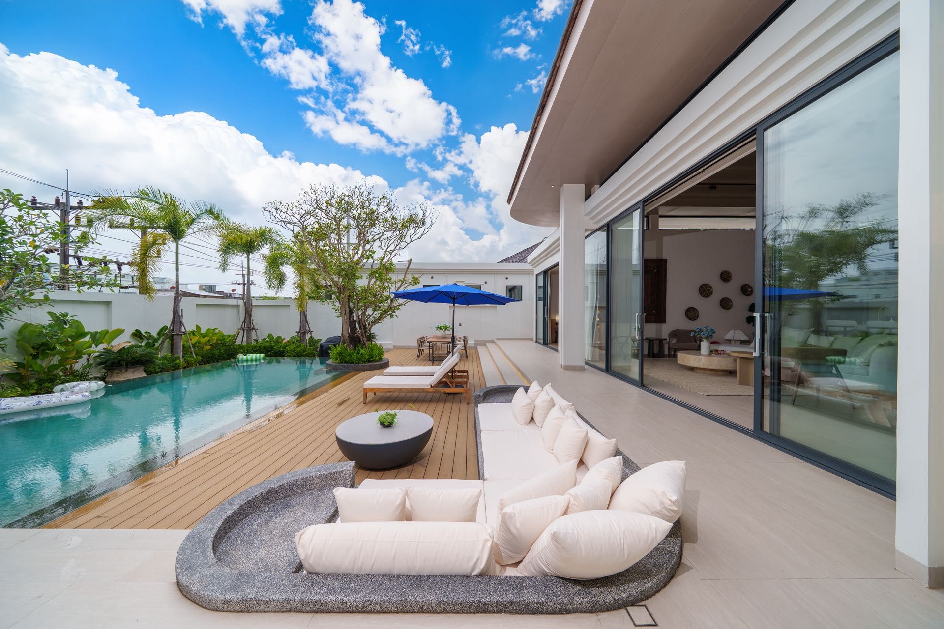 Un área de piscina moderna al aire libre con terraza de madera, sillones de descanso y una zona de estar con una mesa redonda.