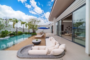 Un espace piscine extérieur moderne, doté d’une terrasse en bois, de chaises longues et d’un coin salon avec une table ronde.