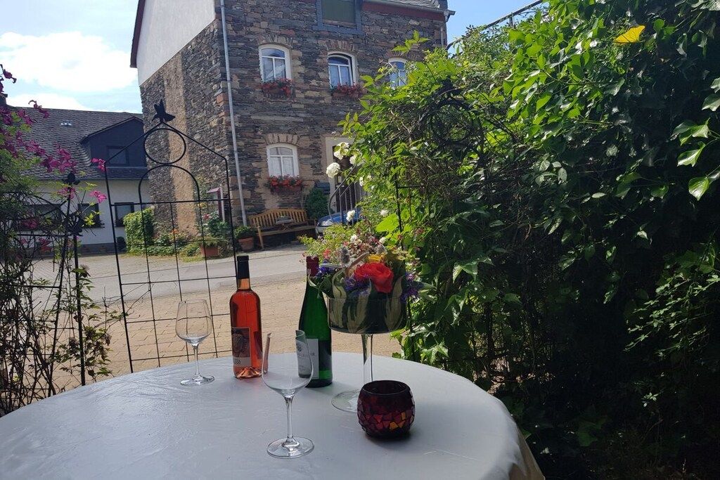 A table with wine glasses and bottles, surrounded by greenery and a stone building in the background.