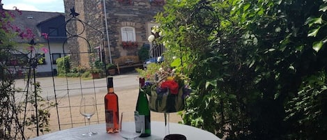 A table with wine glasses and bottles, surrounded by greenery and a stone building in the background.