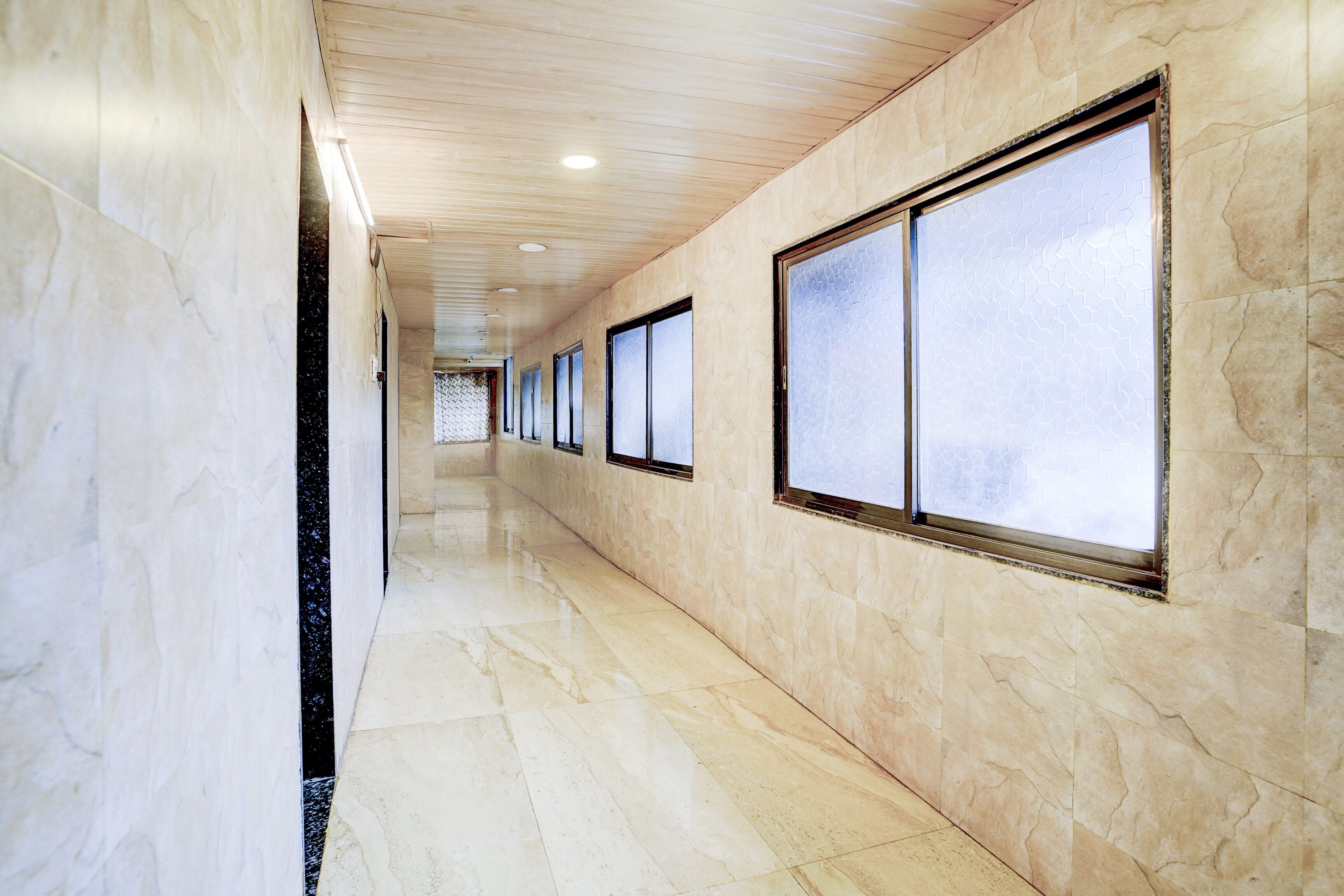 Un pasillo con paredes y piso de mármol, ventanas amplias e iluminación empotrada en el techo.