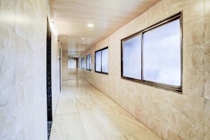 A hallway with marble walls and floor, large windows, and a ceiling with recessed lighting.