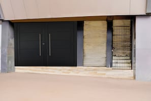 A closed black double door with a metal handle, a metal gate with horizontal bars, and a concrete floor.