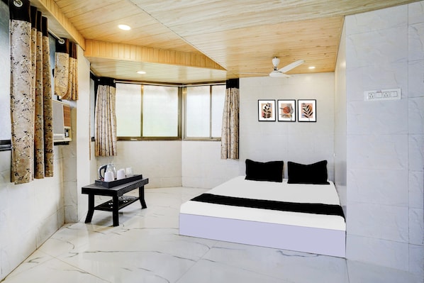 A bedroom with a bed, a table with cups and a kettle, a window with curtains, and wall-mounted artwork. - Hotel O Chopda Court Ulhasnagar (Ambernath)