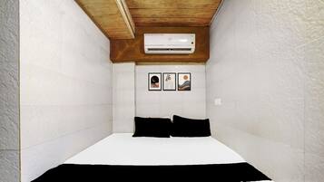 Una habitación pequeña y estrecha con una cama, paredes blancas y un techo de vigas de madera.