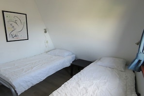 Ein Zimmer mit zwei Einzelbetten, einem kleinen Tisch und einem an der Wand hängenden Bild.