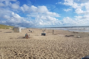 A sandy beach with a few structures, including a small shelter and a wooden bench. - Holiday apartment with 2 bedrooms (Julianadorp)