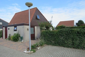 A residential building with a tiled roof, a small attached structure, a paved driveway, and a hedge. - Holiday apartment with 2 bedrooms (Julianadorp)