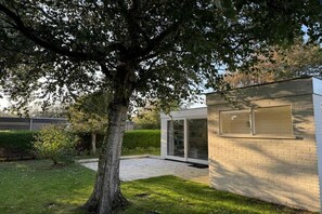 A modern building with a glass facade, surrounded by a well-maintained lawn and a large tree. - Beach House Ogentroost (Julianadorp)