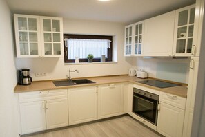 A kitchen with white cabinets, a window with blinds, a sink, a coffee maker, and a toaster. - Holiday apartment with 3 bedrooms (Weisenheim am Sand)