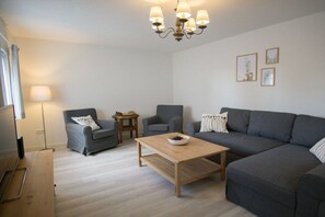 A modern living room with a grey sofa, two armchairs, a wooden coffee table, and a chandelier. - Holiday apartment with 3 bedrooms (Weisenheim am Sand)