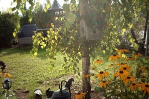 A garden with a birdhouse, a gazebo, and a chair. - Panoramic holiday apartment with lake view (Schalkenmehren)