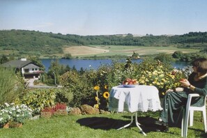 Un cadre idyllique au bord du lac, avec une table et une chaise, une maison en arrière-plan et une vue sur le lac et les collines.