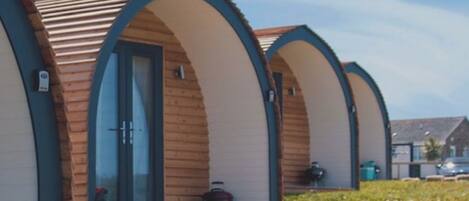 A row of wooden cabins with arched doorways and windows, each with a small porch area.