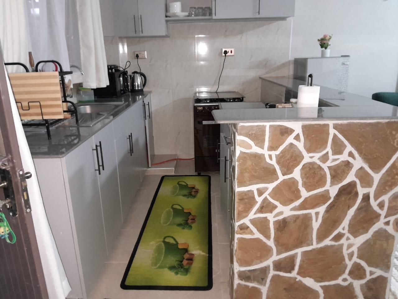 Una cocina con protector contra salpicaduras de piedra, lavavajillas y encimera con diversos electrodomésticos.