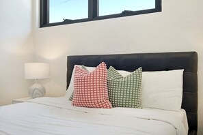 Una cama con edredón blanco y tres almohadones estampados en rojo, verde y blanco.