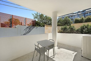 A balcony with a table and chairs, a white wall, and a view of a building and trees. - Elegant Urban Retreat in the Heart of Epping (Epping)